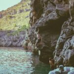 A group of people standing on the side of a cliff next to a body of