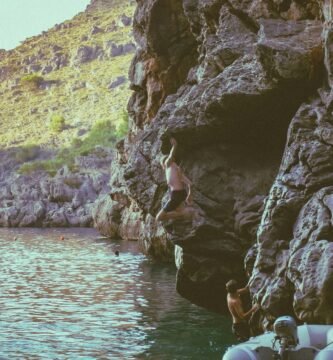 A group of people standing on the side of a cliff next to a body of